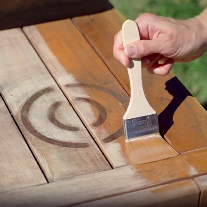 Person applying wood stain to a wooden surface with a brush