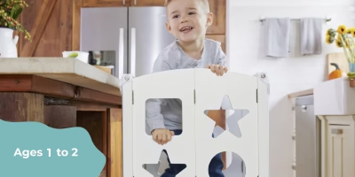 Smiling toddler stands behind a white baby gate in a bright kitchen, with text that reads Ages 1 to 2 and safety at home.