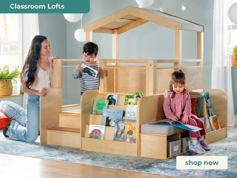 A large wooden children's loft bed with integrated bookshelves and stairs, shown in a bright room with two children and an adult interacting with it. A teal banner at the top left reads 'Classroom Lofts' and a white 'shop now' button appears at the bottom right.