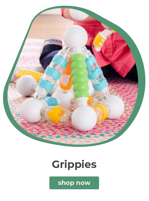 A child wearing a pink shirt sits on a patterned rug indoors while playing with a colorful plastic toy structure labeled 'Grippies' and a green 'shop now' button below on a white background.